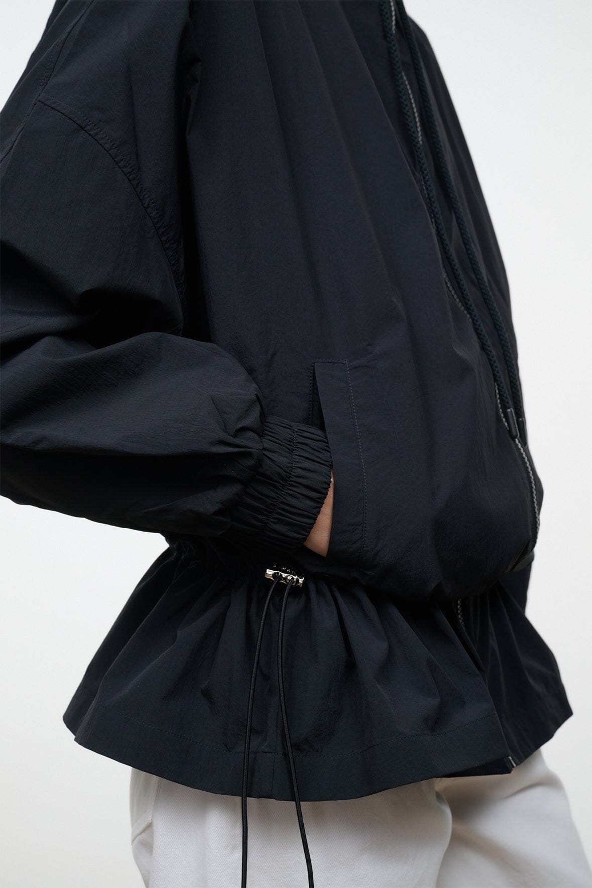 Black hooded jacket close-up: gathered drawstring hem and elastic waist detail.