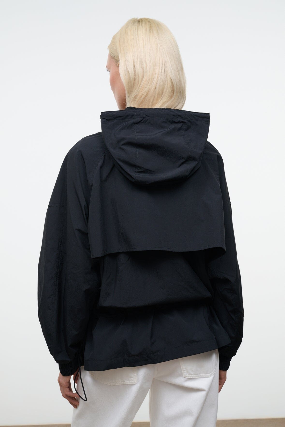Black hooded wind jacket, back view with draped collar and drawstring hem