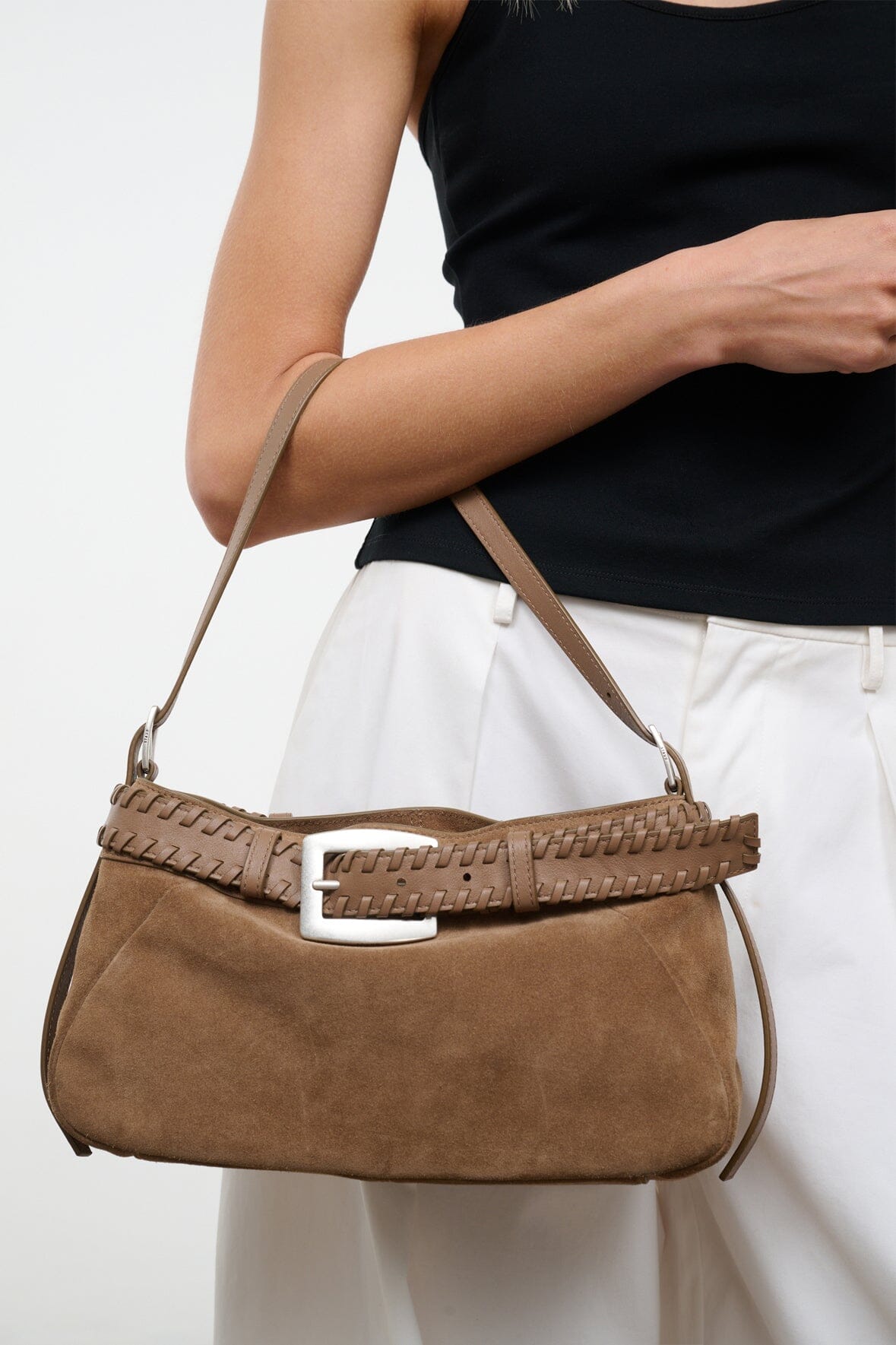 Tan suede shoulder bag worn on shoulder with woven trim and silver buckle