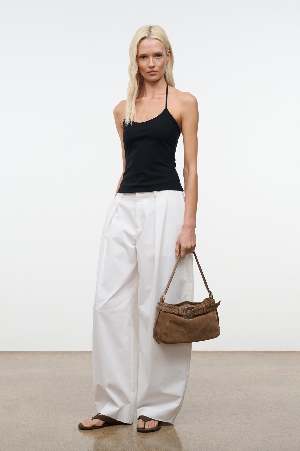 Tan suede shoulder bag with woven strap trim and silver buckle, held at side