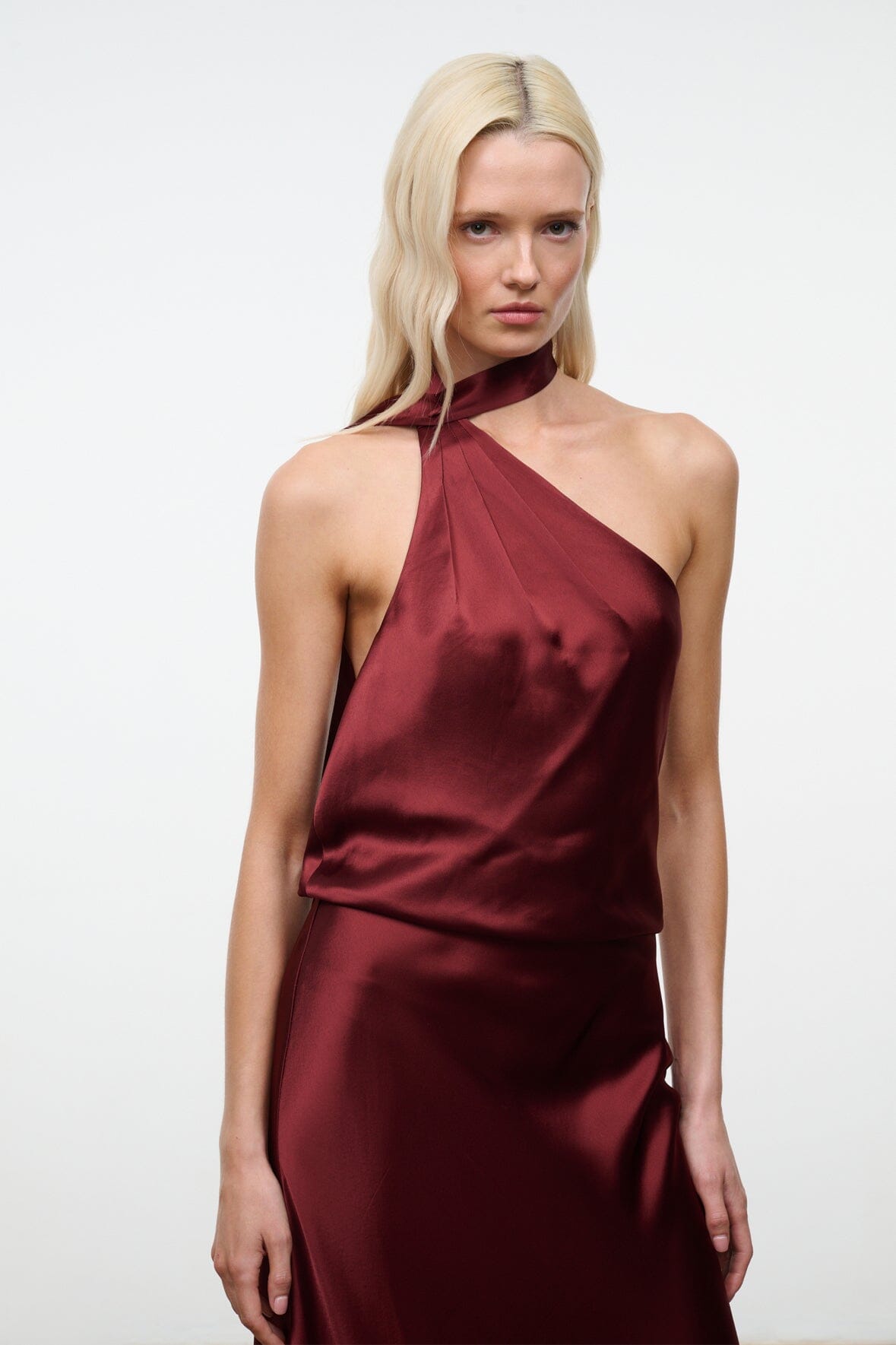 Wine satin halter dress with draped one-shoulder neckline, sleeveless, bias silhouette.
