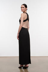 A woman modeling a floor-length black dress with a dramatic open back and halter-style shoulder straps, shown from the back in a studio setting.