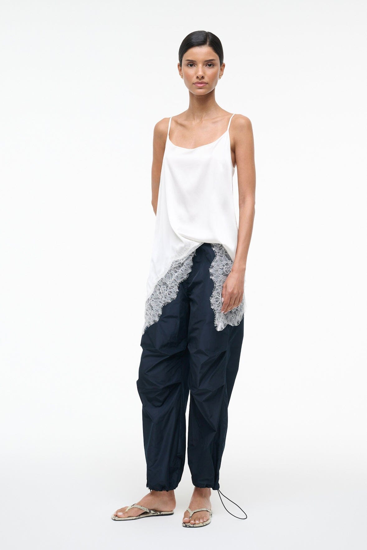 Woman wearing snake-print thong sandals with navy pants and white lace hem