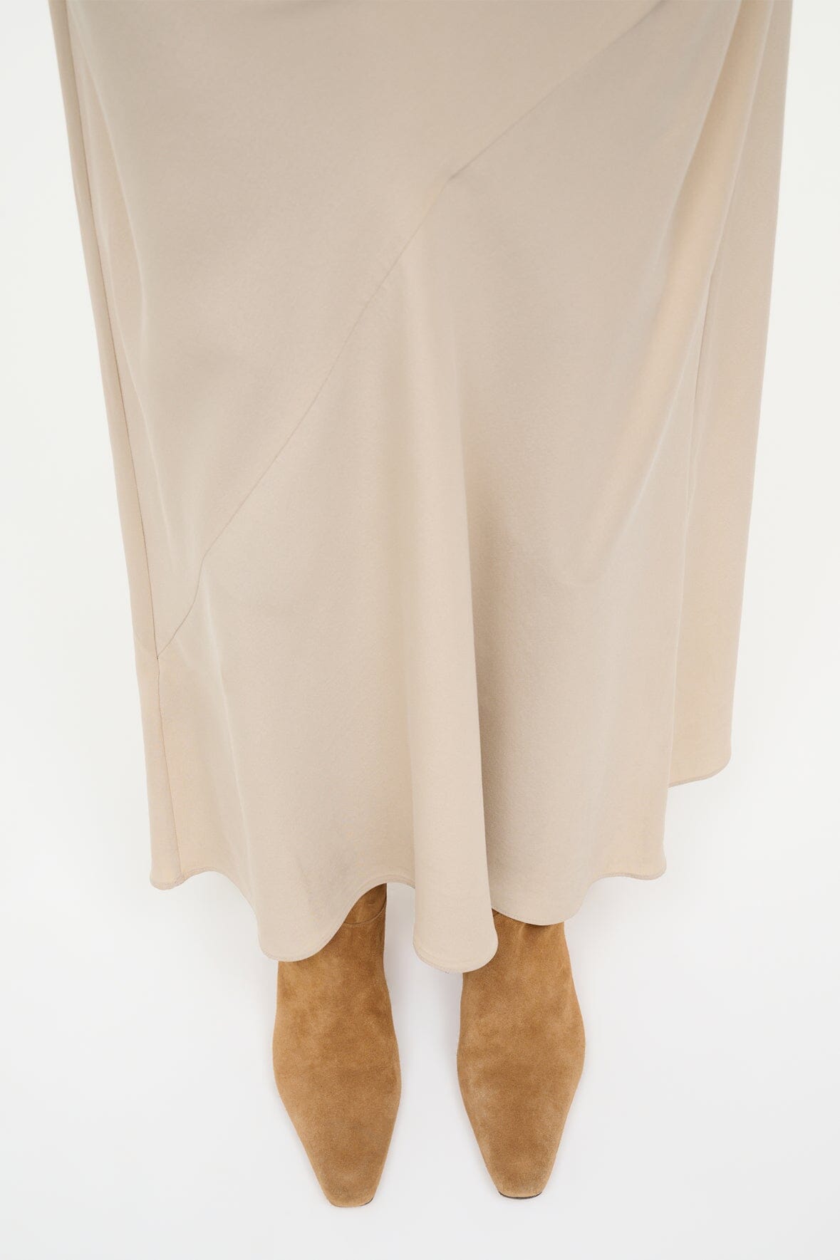 Tan suede western boots with low heel under a cream dress hem