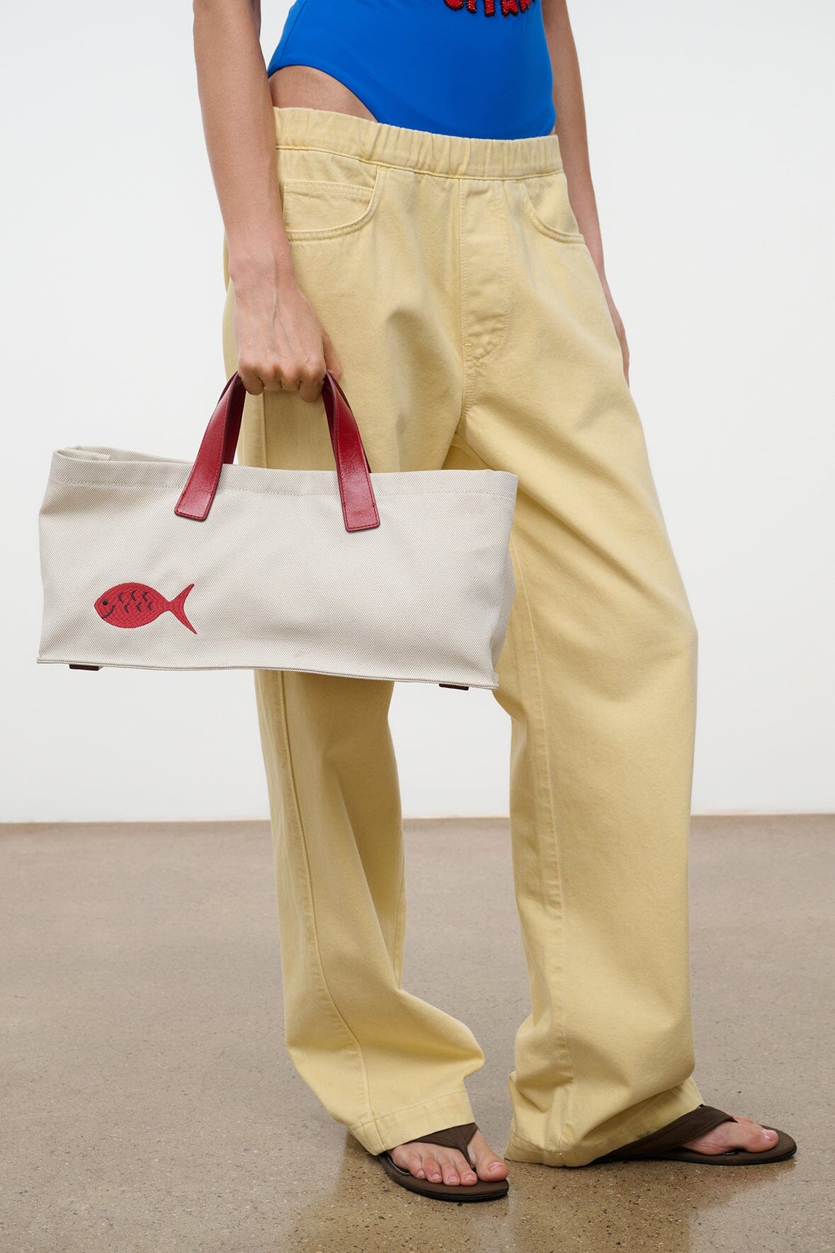 Cream tote bag with red fish applique and red handles, carried while seated