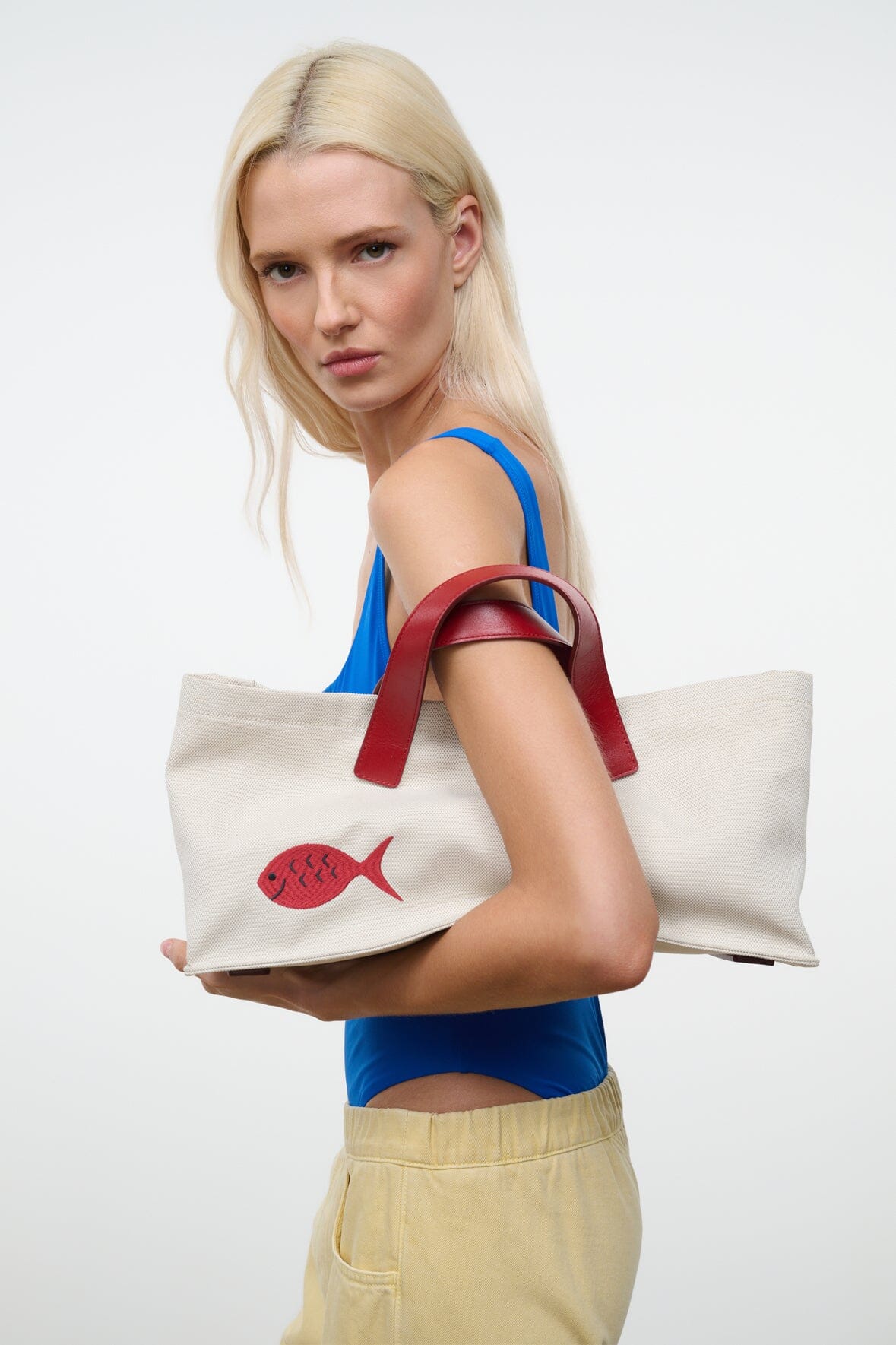Cream tote bag with red handles and red fish applique, held at the side