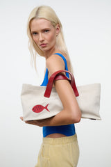 Cream tote bag with red handles and red fish applique, held at the side