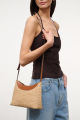 Natural tan raffia shoulder bag with long crossbody strap and scalloped trim.