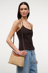 Tan raffia crossbody bag with long strap and scalloped top edge.