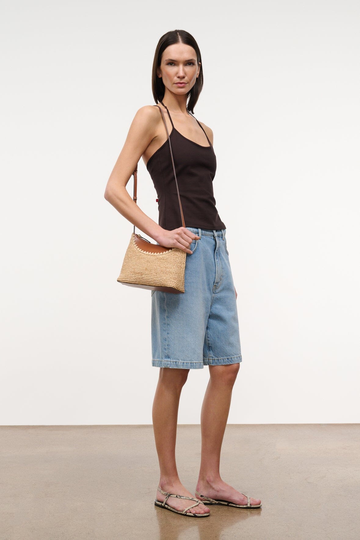 Tan raffia shoulder bag with long strap and scalloped top edge.