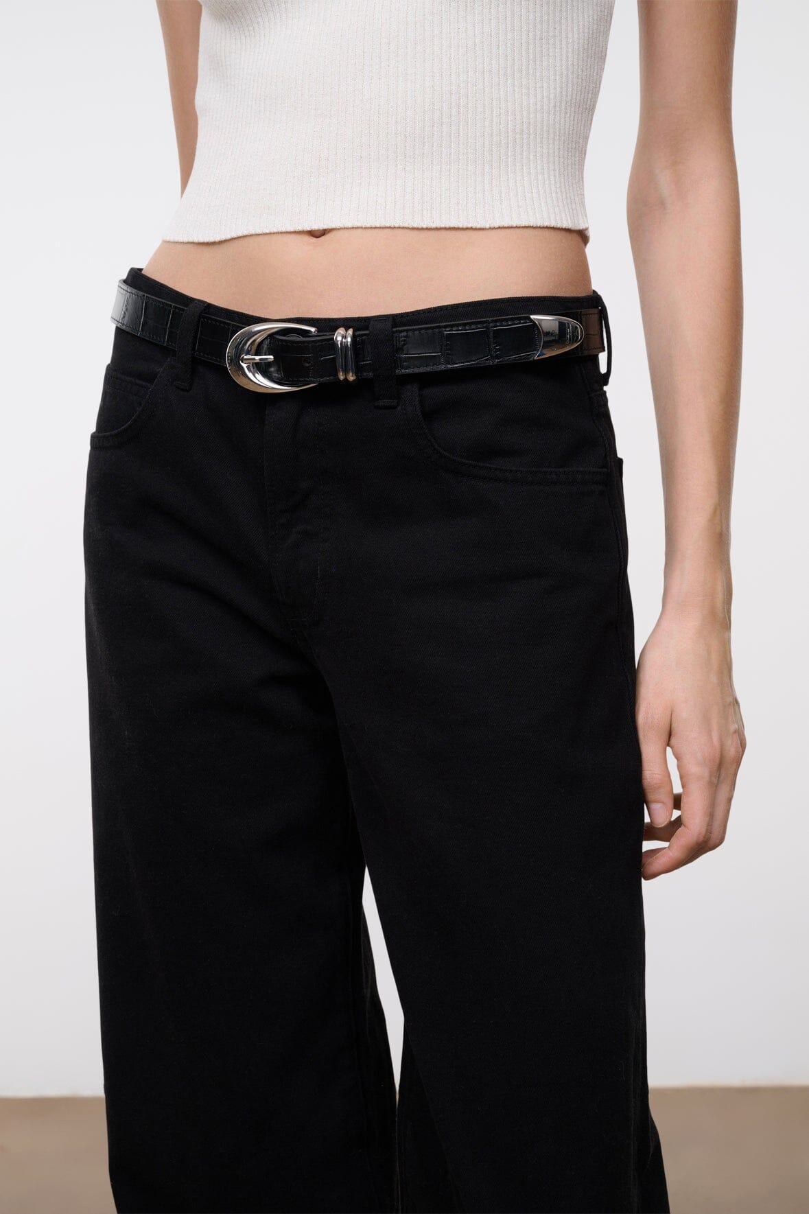 Black croc-texture belt with silver oval buckle on dark jeans.