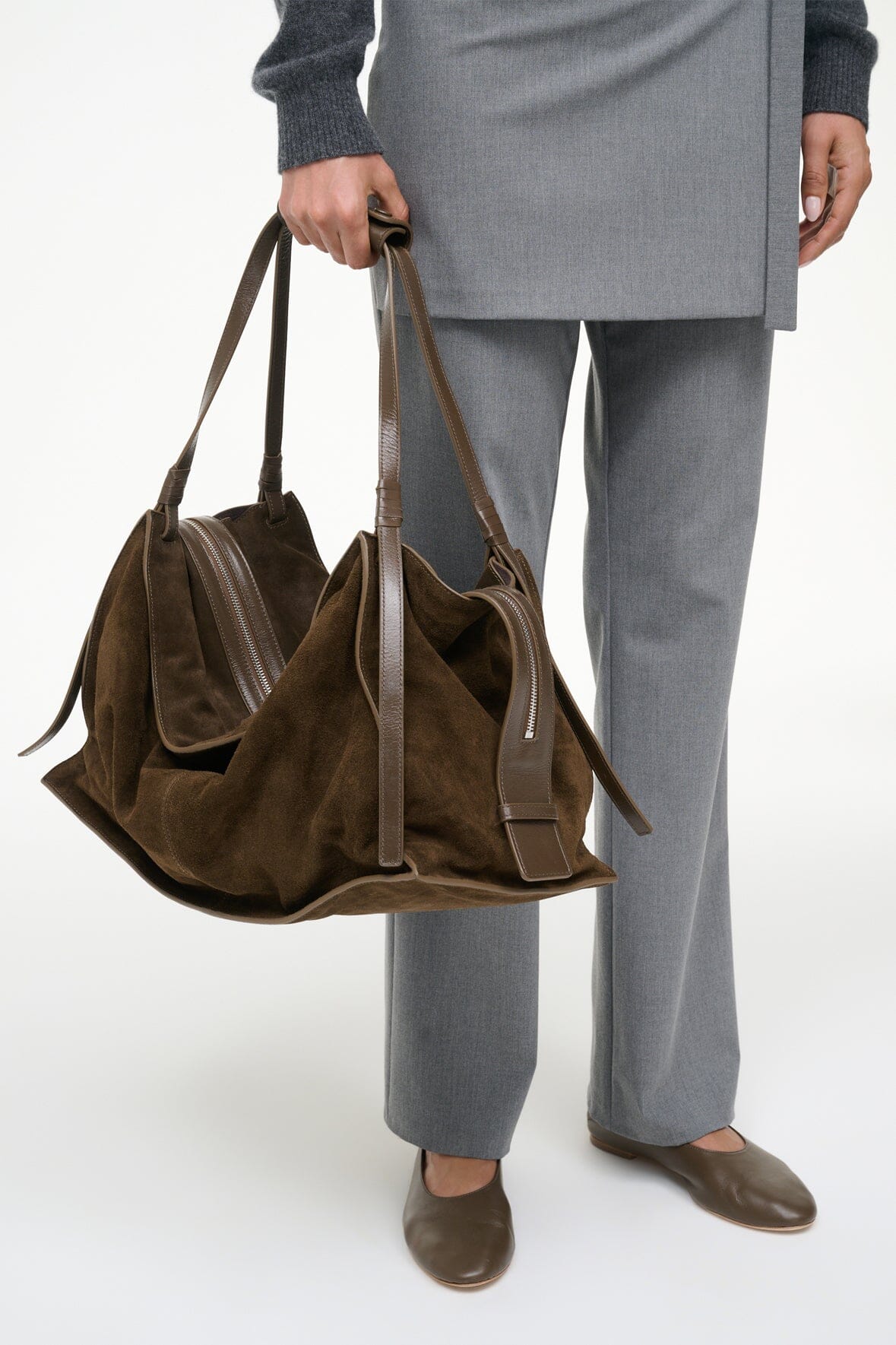 Truffle suede tote bag held by top handles with front zip pocket and tassels