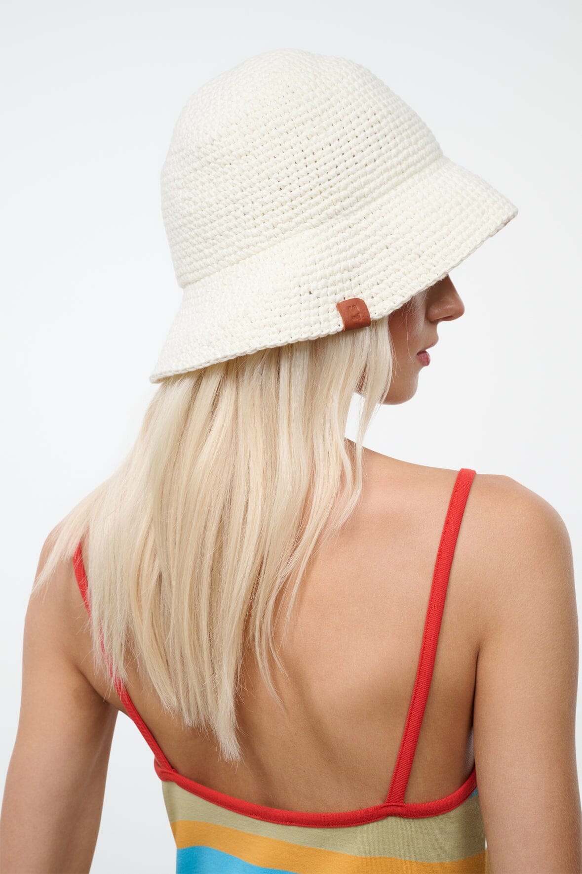 Off-white crochet bucket hat with wide brim and brown side tag; worn from the side.