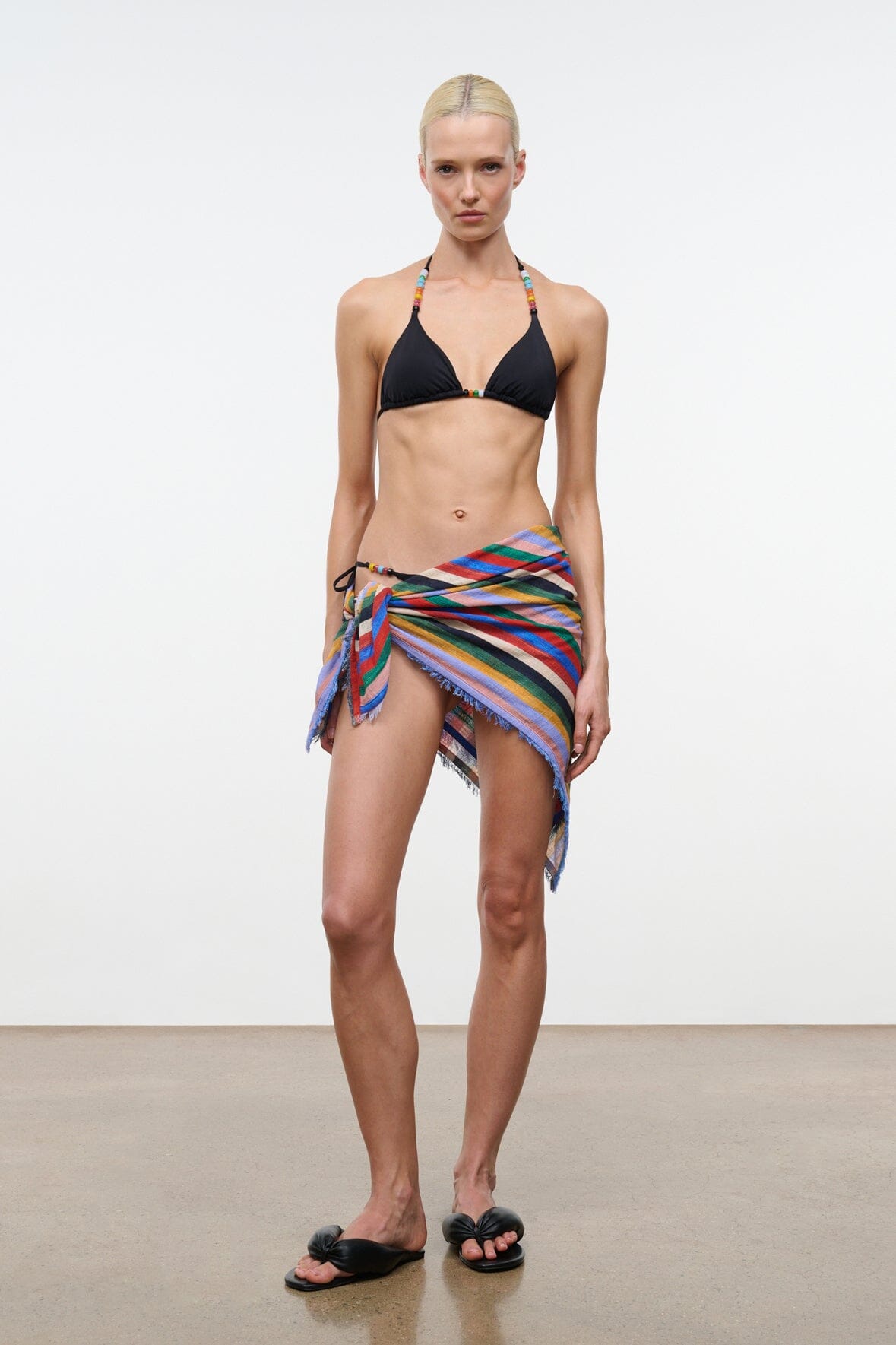 Black triangle bikini top with tie neck, worn with a colorful wrap skirt.
