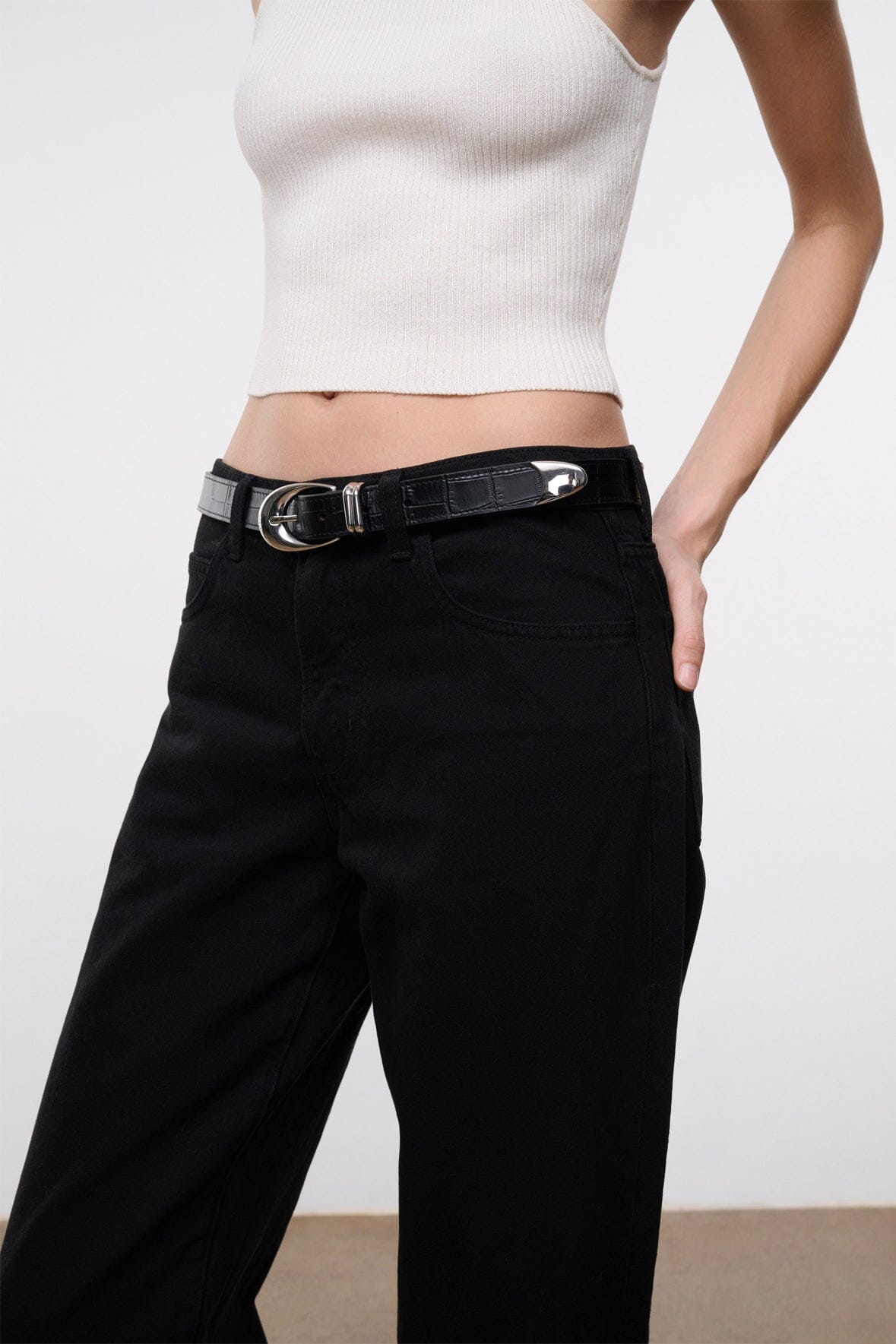 Black croc-texture belt with silver oval buckle at pant waist.