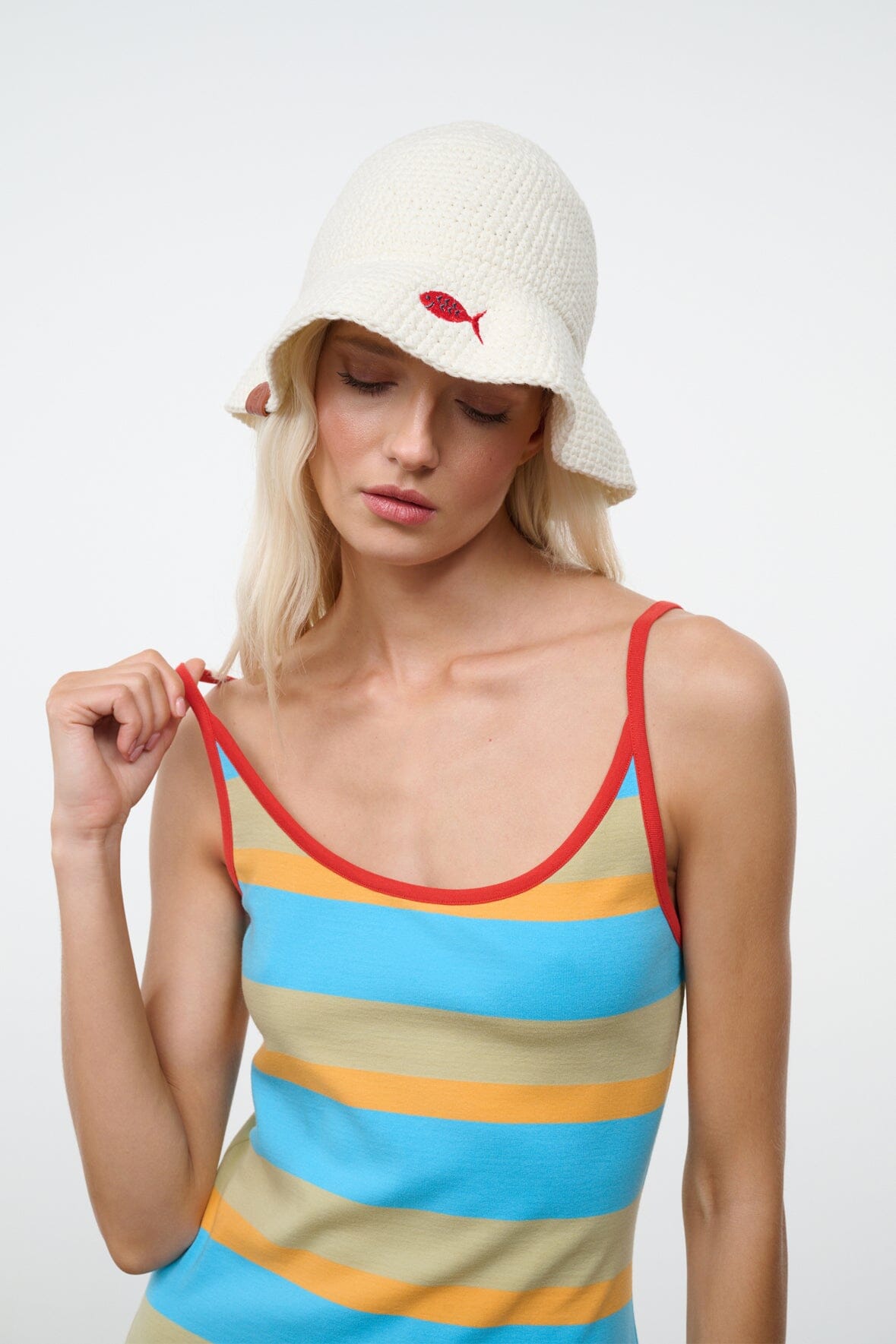 Off-white crochet bucket hat with wide brim and brown side tag; model adjusting strap.
