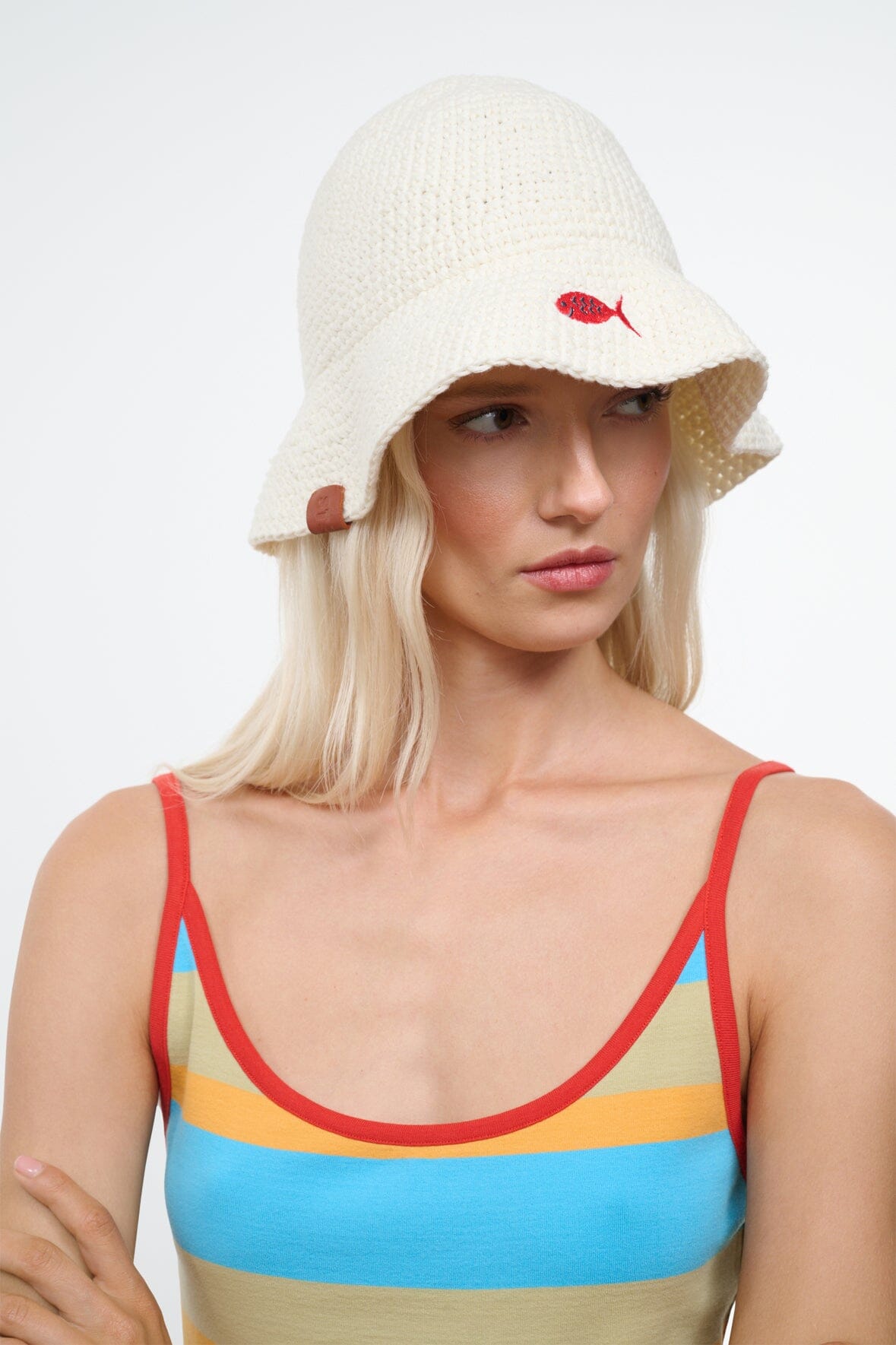 Off-white crochet bucket hat with red fish emblem and brown side tag; front view.