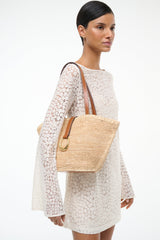 Natural tan woven tote bag side view with tan leather handles and front pocket tab