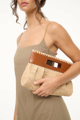 Natural tan straw clutch with brown leather flap and rectangular opening, held to side.