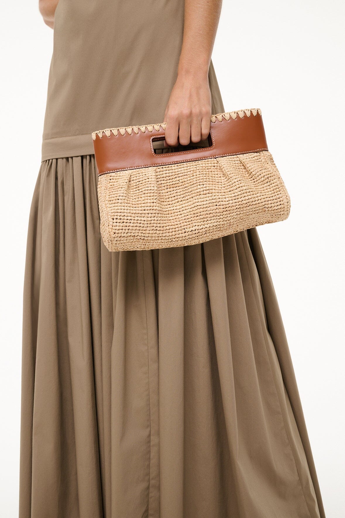 Natural tan woven clutch held by hand with brown leather top flap and handle.