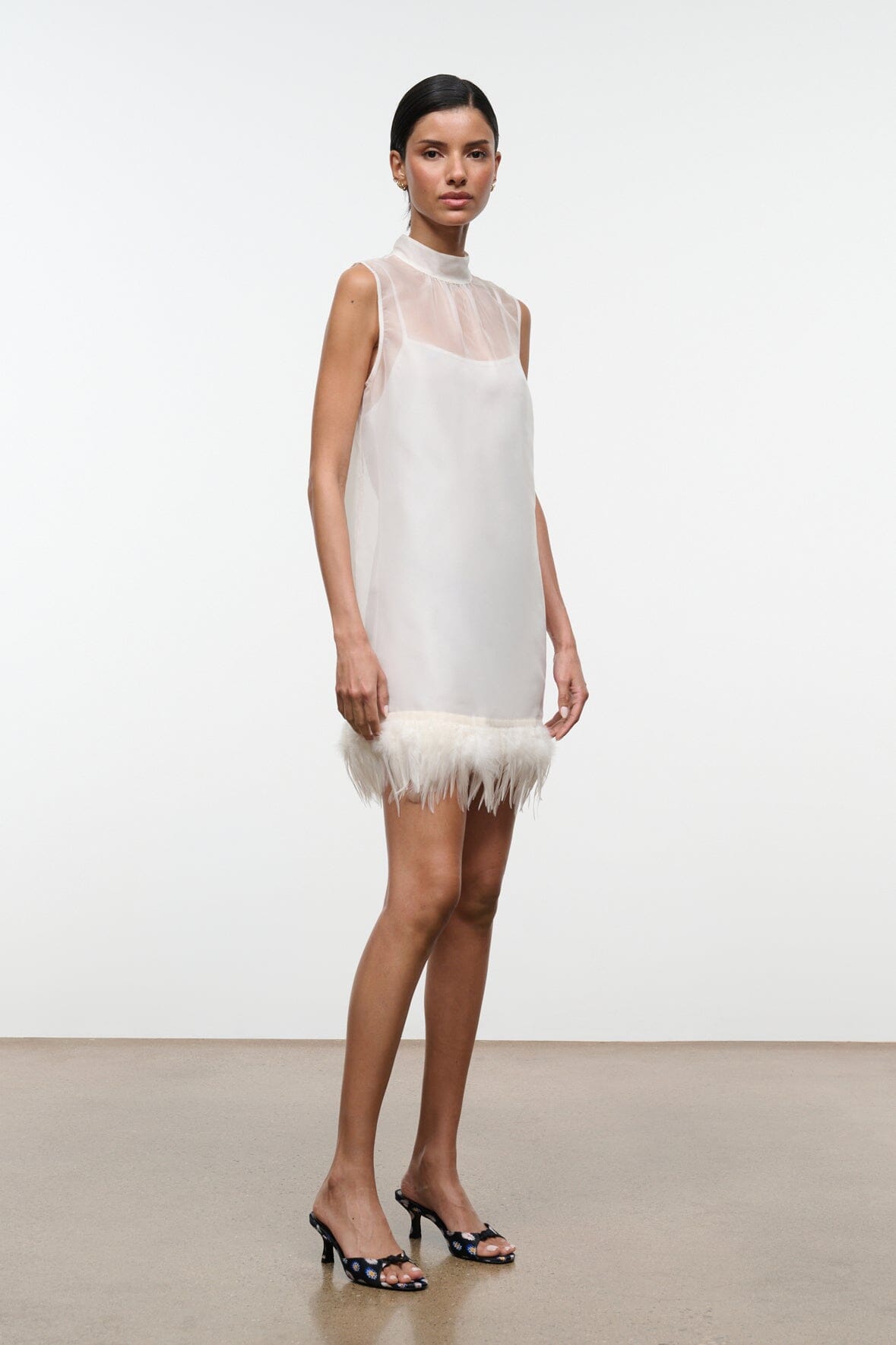 Ivory sleeveless mini dress with high neck and feather trim at the hem