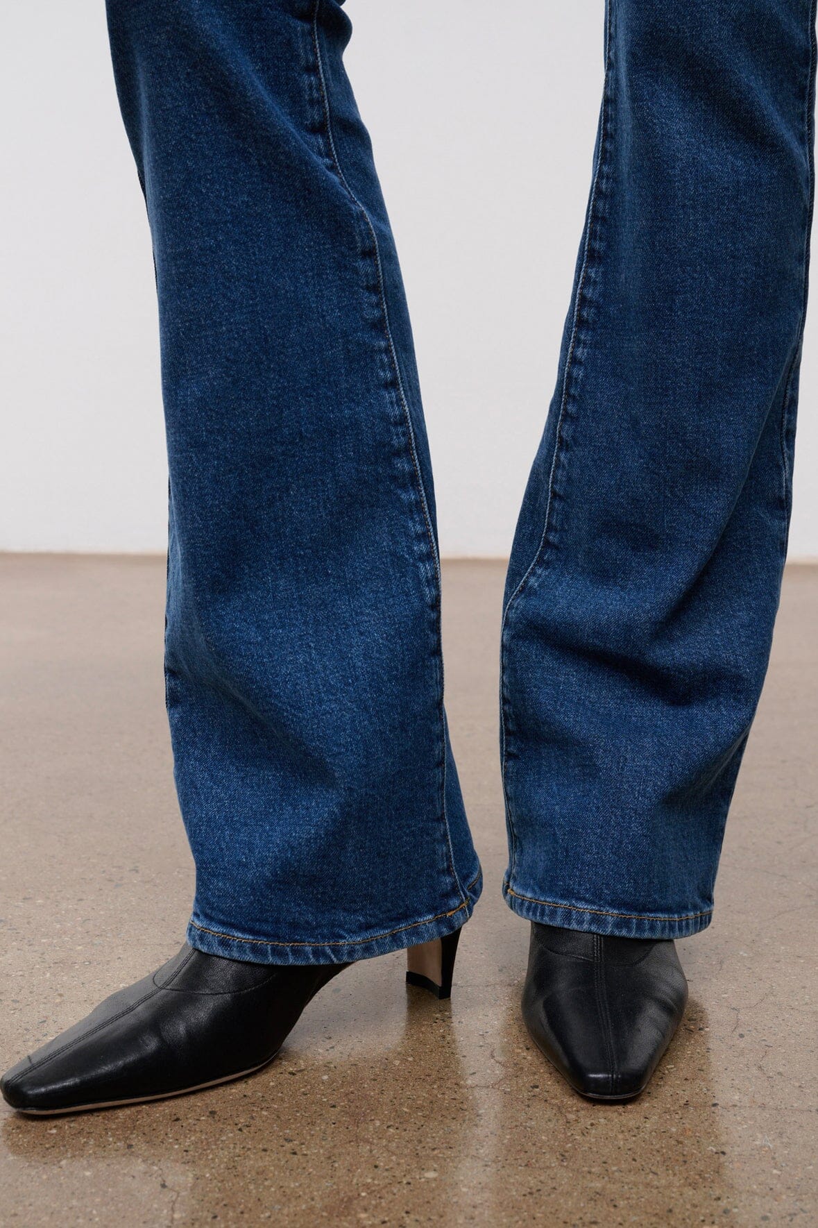 Women's stone blue flare jeans with stitched hem and wide bell opening over black boots