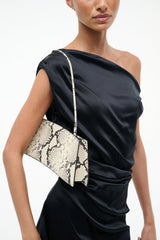 White snake-pattern shoulder bag front with wide diagonal strap over dress
