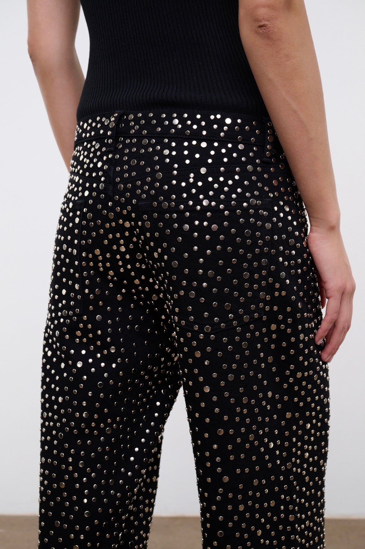 Black relaxed jeans with silver studs covering the front; visible waistband and hip.