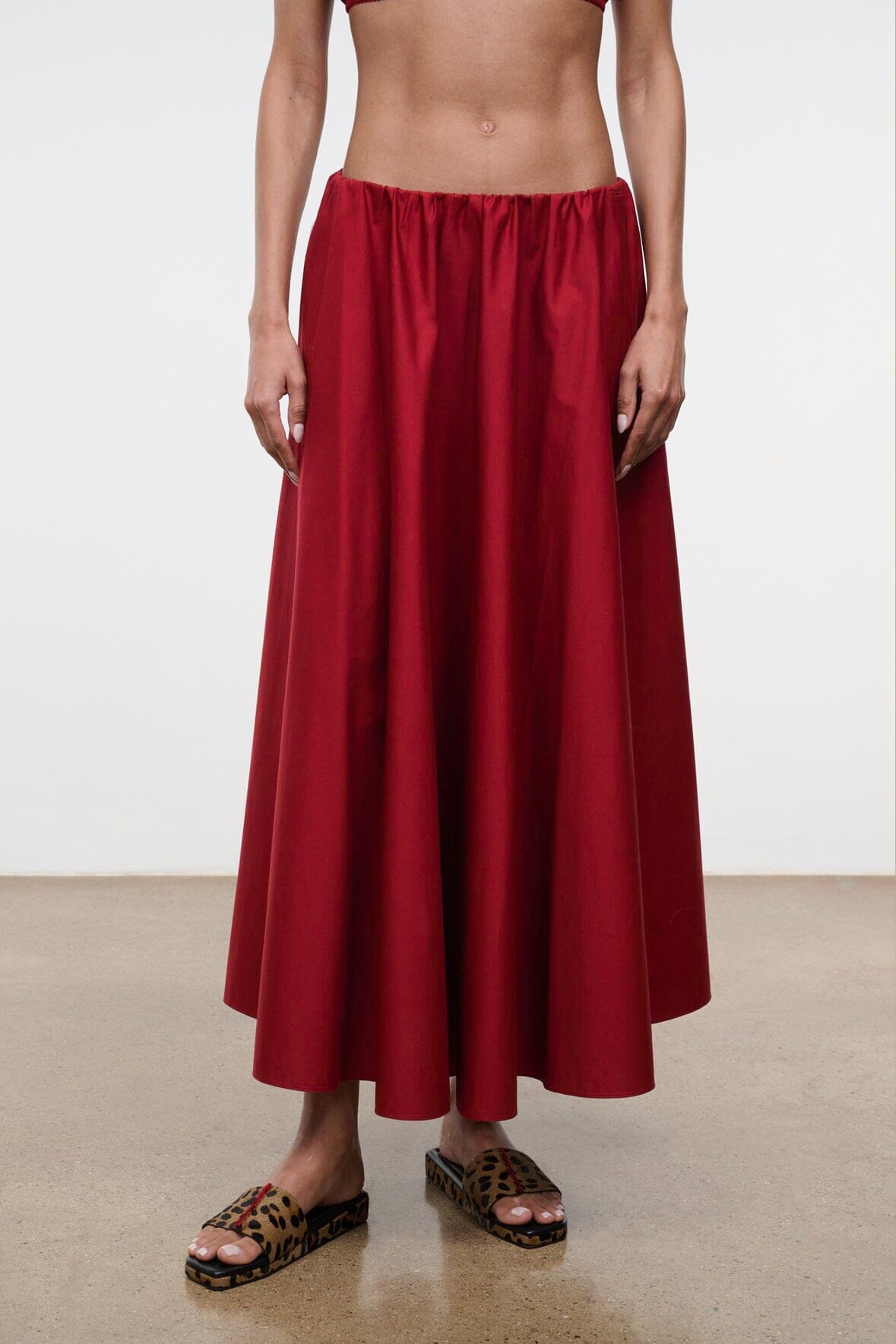 Close-up of red midi skirt with gathered elastic waistband and pleated fabric