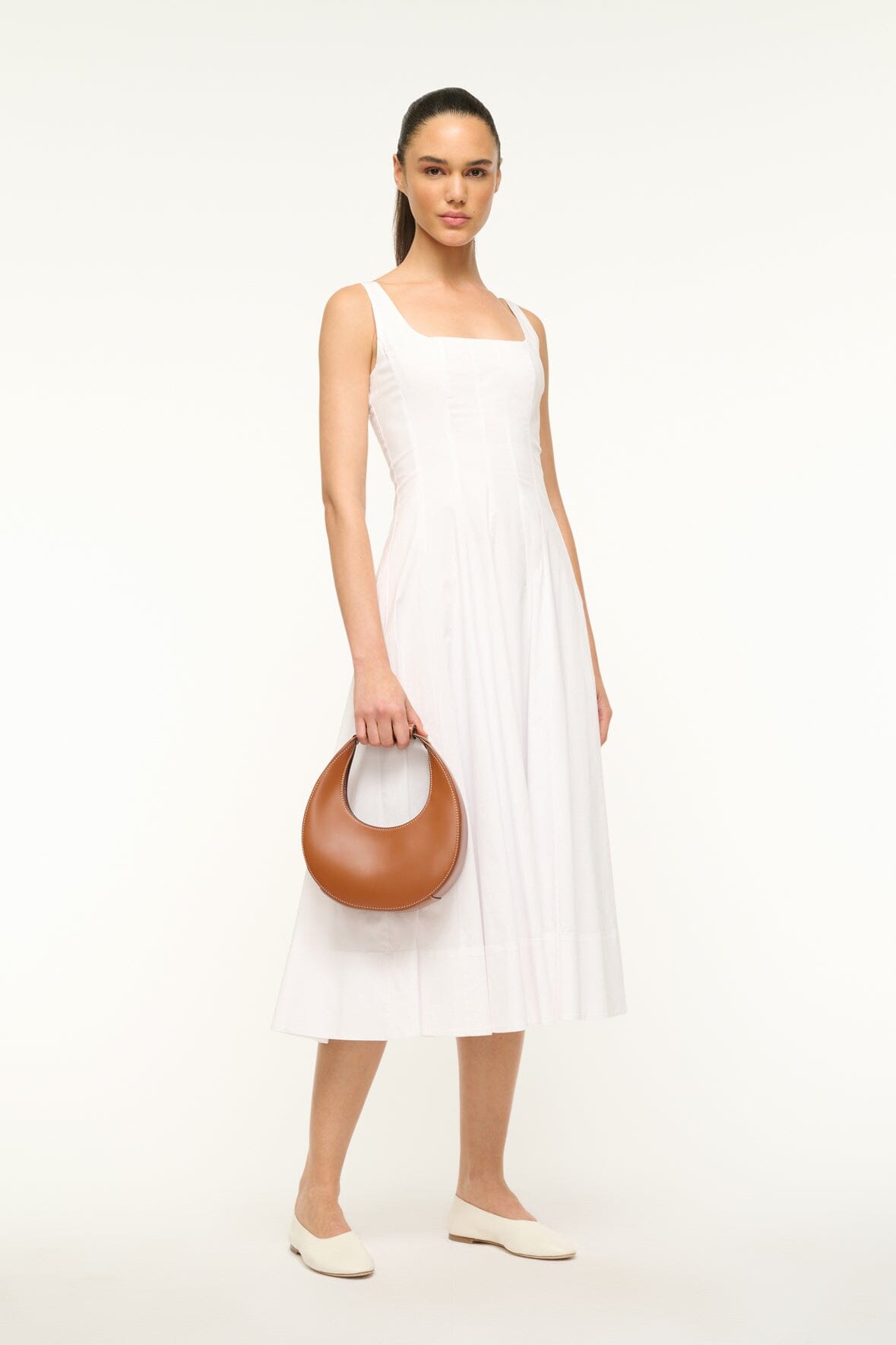Mini moon bag tan leather worn crossbody with curved top and short strap.