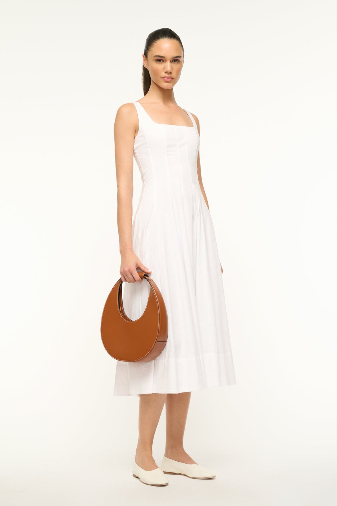 Saddle brown leather half-moon bag held at hip by model