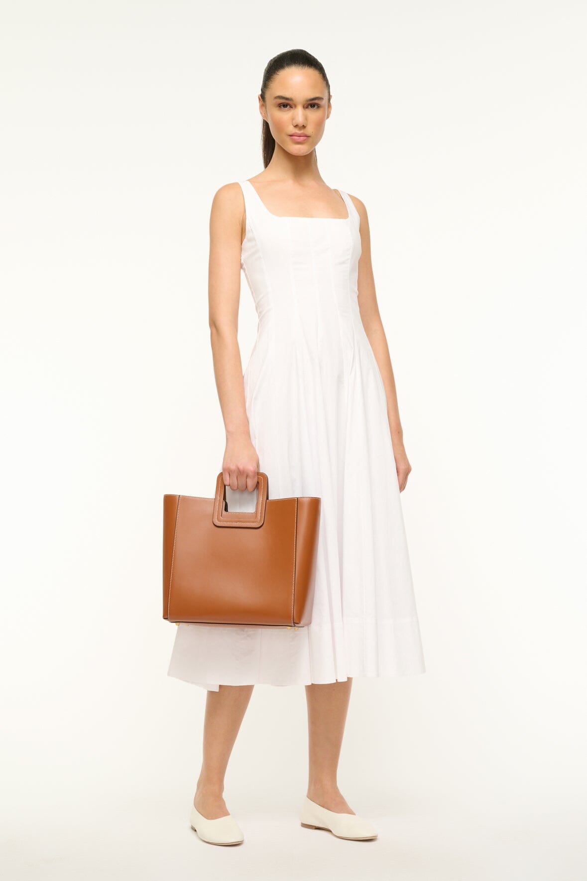 Tan leather bag held in hand with top handle and compact pouch shape