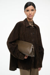 Truffle-brown soft clutch bag with top zipper, held at chest level