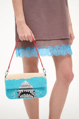 Turquoise sequin shoulder bag held by red strap with shark graphic front.