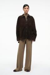 Dark brown suede button-up shirt with pointed collar and flap pocket, worn with beige trousers.