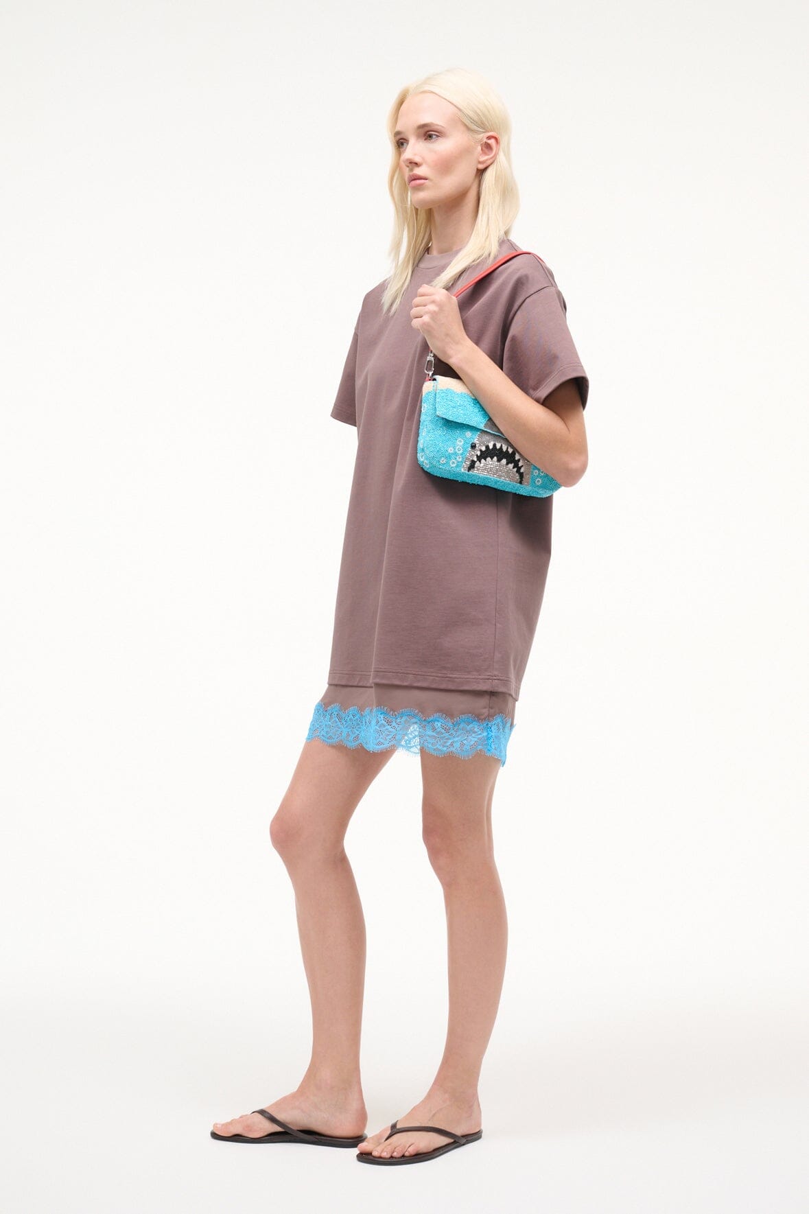 Turquoise sequin shoulder bag on model with red strap and shark artwork.