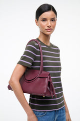 Maroon leather shoulder bag worn with curved top handles and side bows