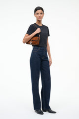 Espresso suede shoulder bag held in hand by model with braided trim