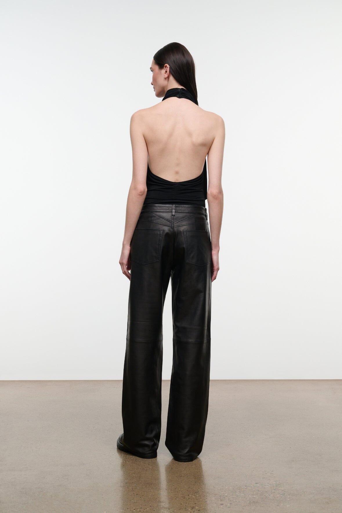 Back view of black leather pants with straight wide legs and center seam