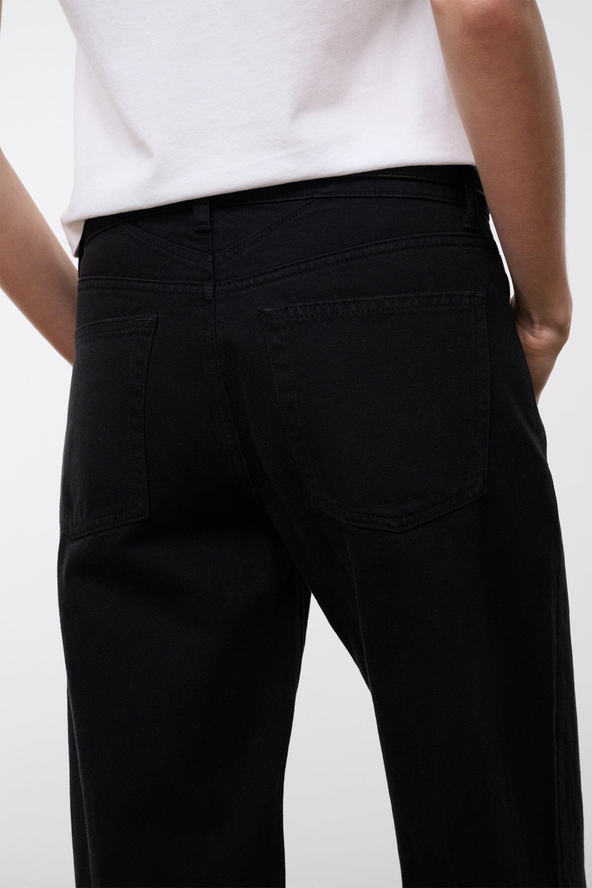 Black relaxed jeans close-up with stitched seam and rear pocket detail, wide leg