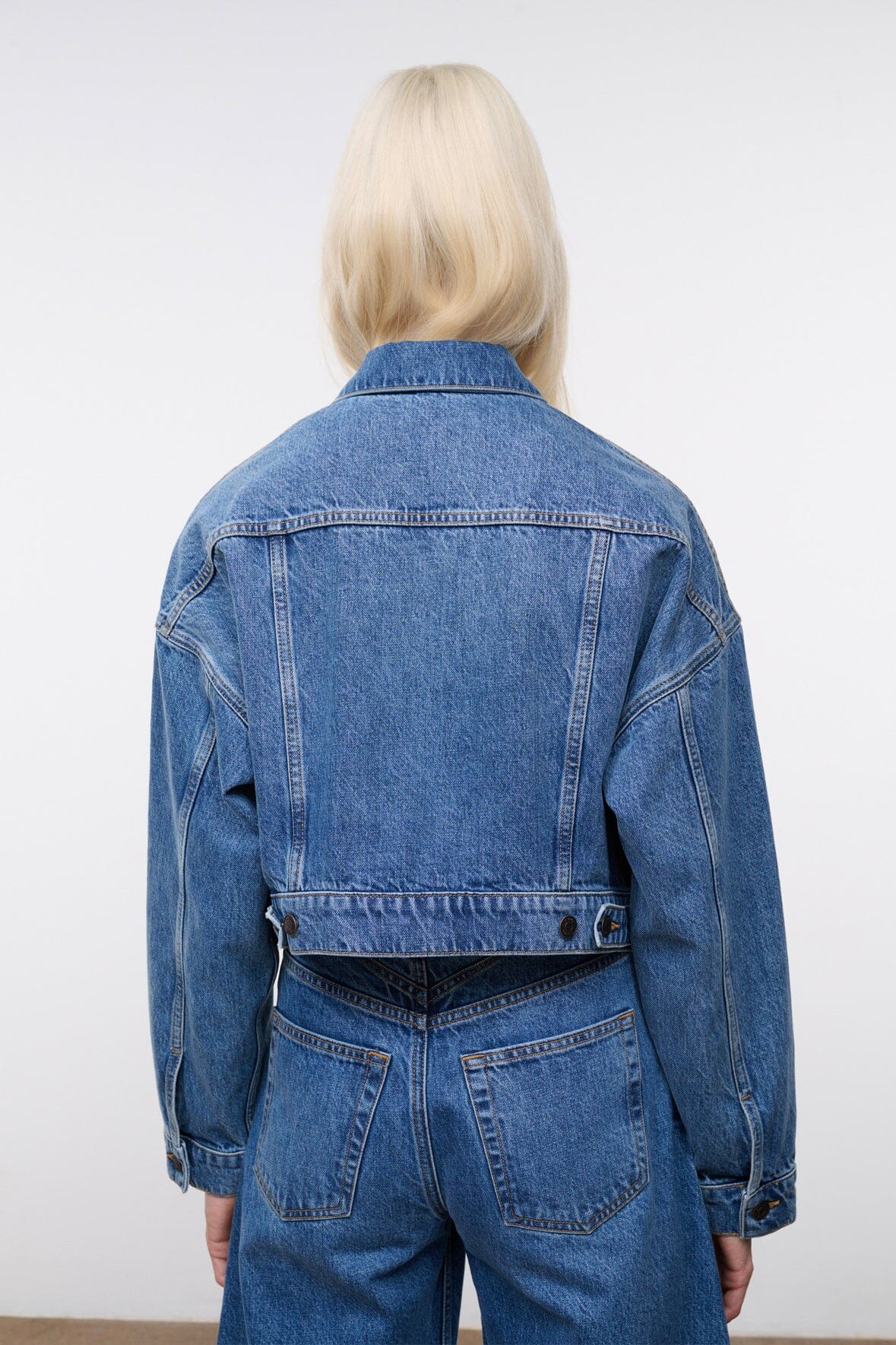 Vintage-wash blue denim jacket back view with yoke seam, button cuffs, patch pockets