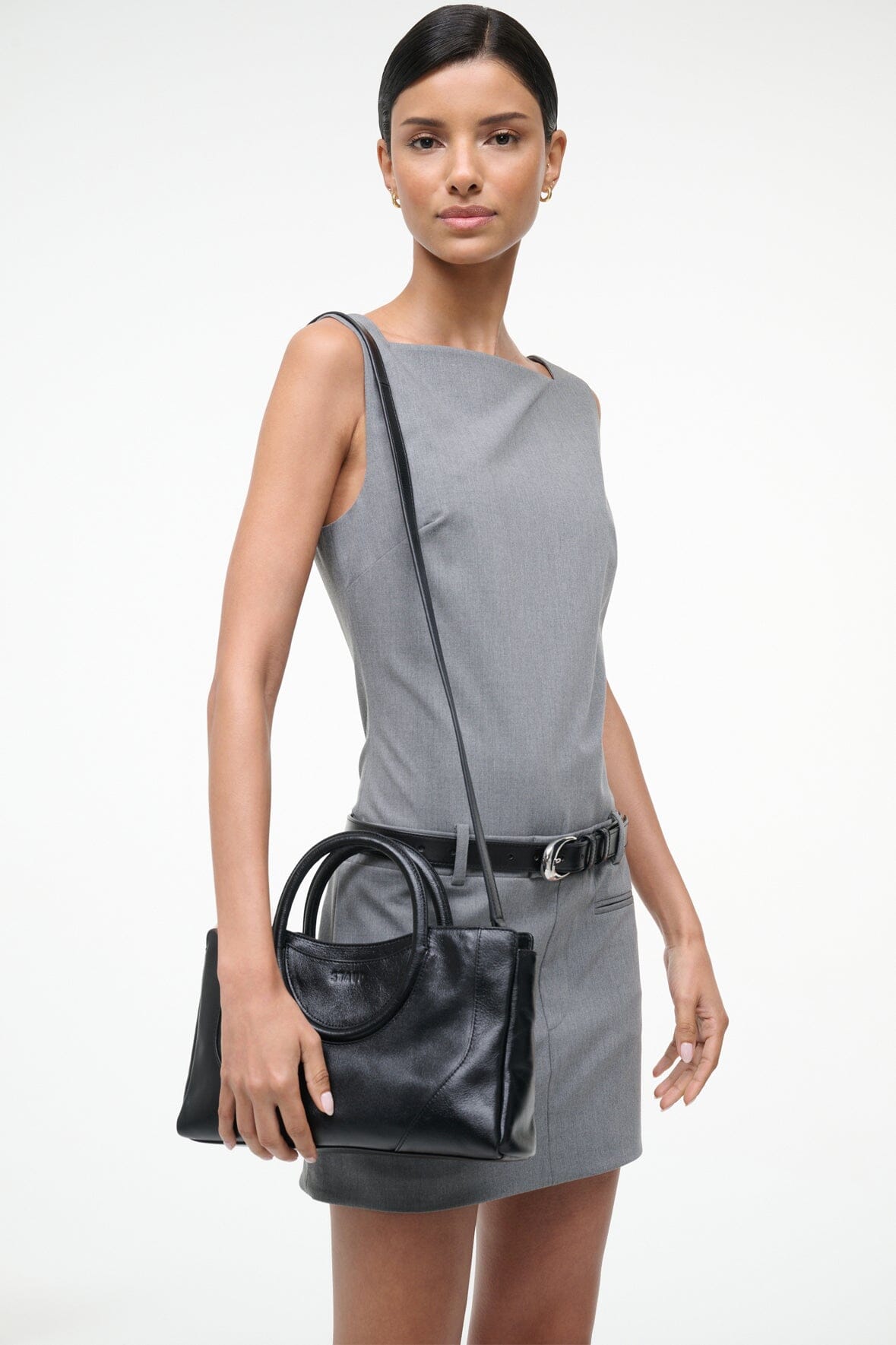 Black mini satchel bag worn crossbody with adjustable strap and top handles