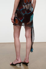 Short asymmetrical mini skirt with sheer side drape; dark teal and orange butterfly print.
