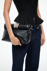 Black leather cuff clutch bag with rolled top flap and wrist strap, carried at front