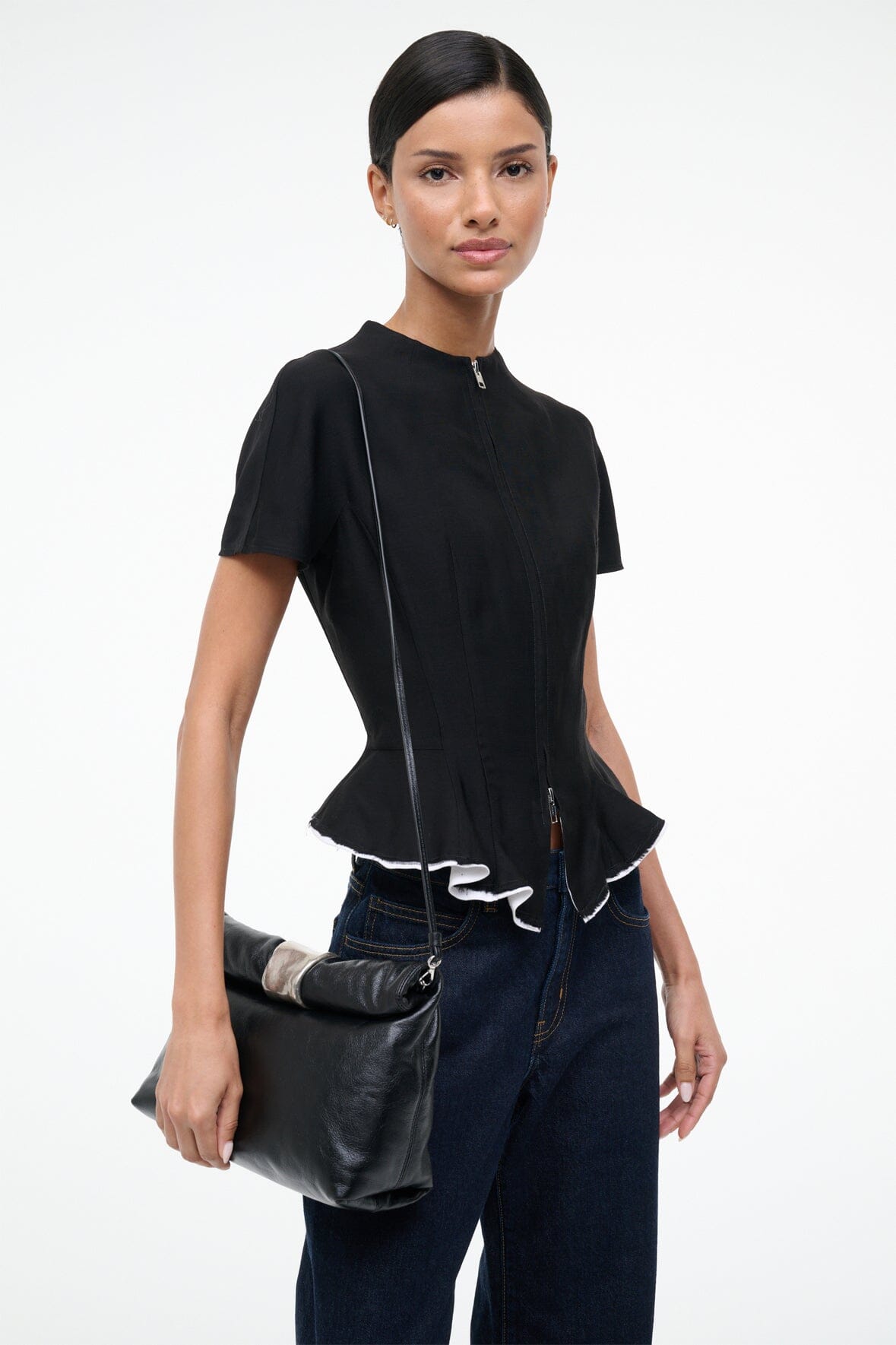 Black leather cuff clutch bag with folded flap and silver clasp, held at side