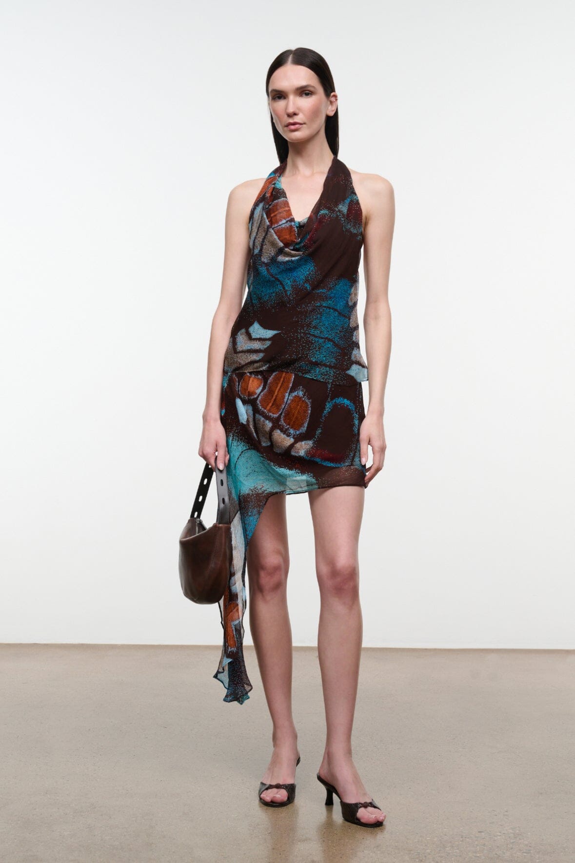Short asymmetrical mini skirt with long sheer drape; butterfly print in teal, orange, and dark tones.