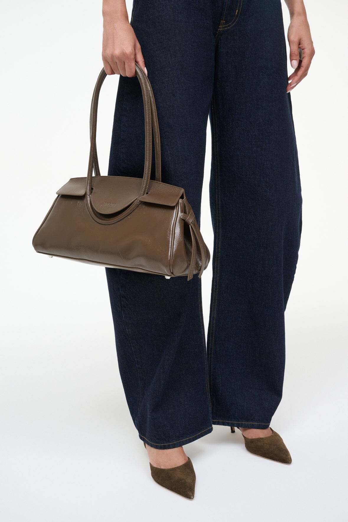 Truffle Maude shoulder bag held at side; structured brown leather with top handles