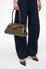 Truffle Maude shoulder bag held at side; structured brown leather with top handles