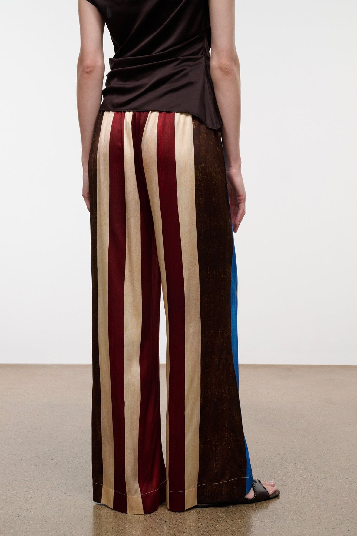Silk pants with vertical burgundy, cream, and brown stripes, shown from the back.