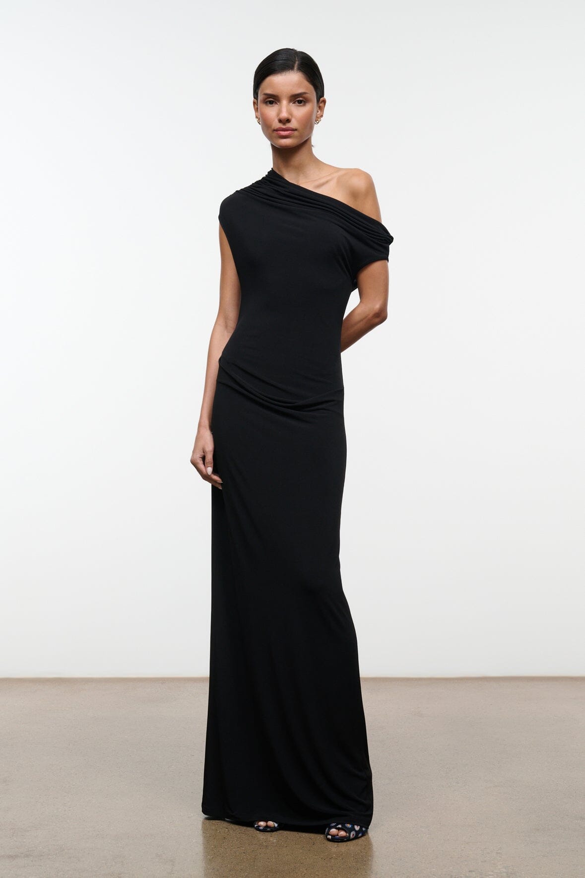 Black one-shoulder draped maxi dress, sleeveless, side view with floor-length skirt